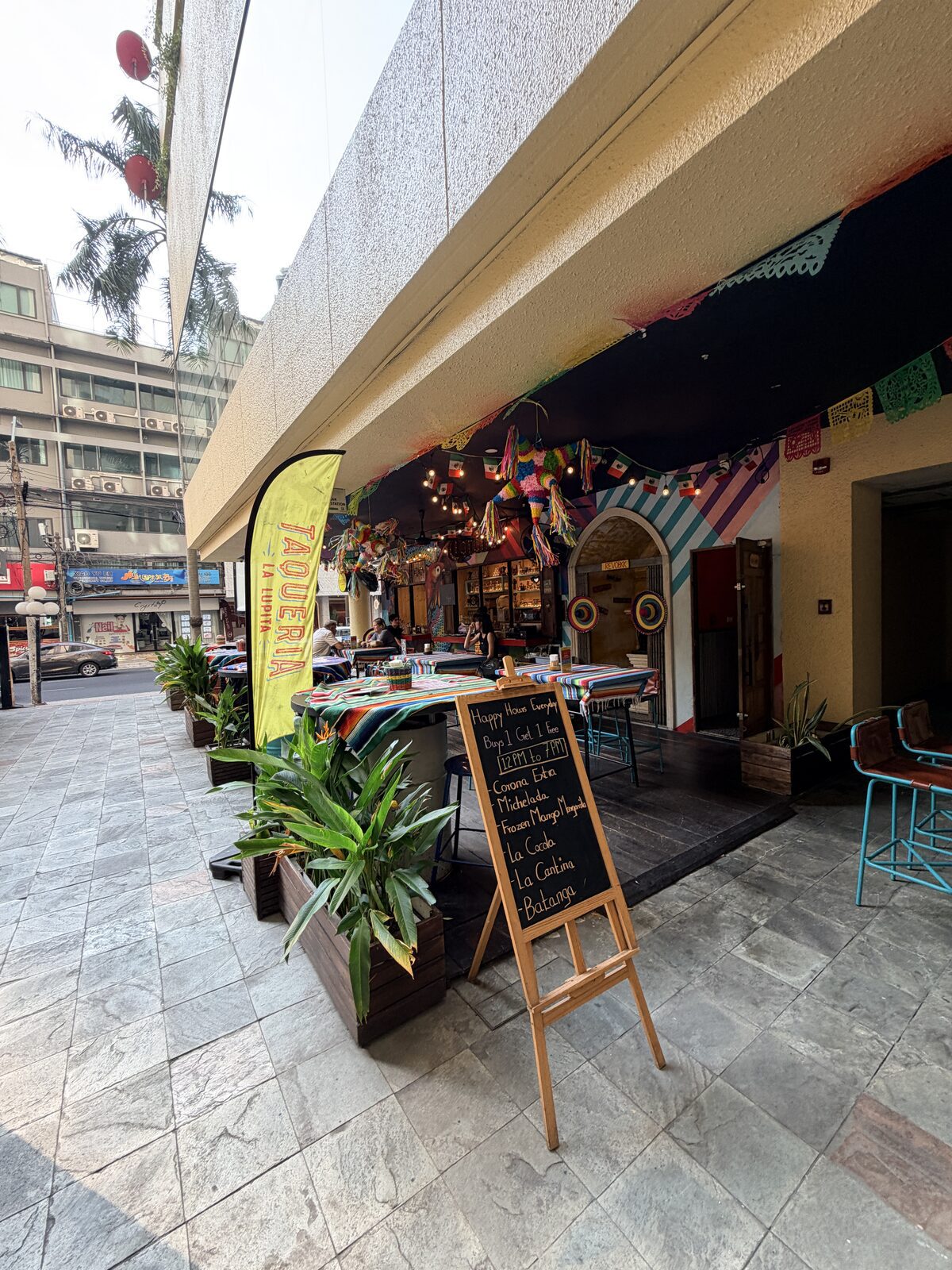 La Lupita Bangkok 半戶外餐廳入口，門口有彩色旗幟、黑板與高腳椅