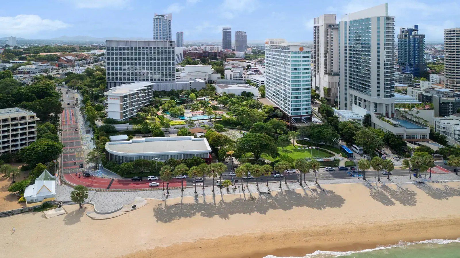 空拍海灘路與沙灘，路旁一排椰子樹，後方是芭達雅市區的高樓