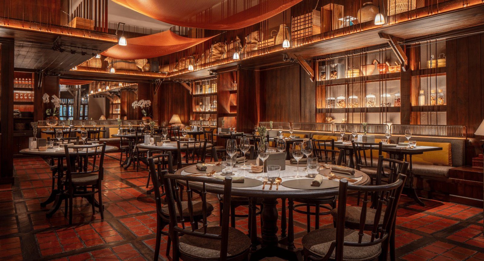 The Spice Market 的木質用餐區，圓桌擺好餐具，牆邊是木櫃與書架