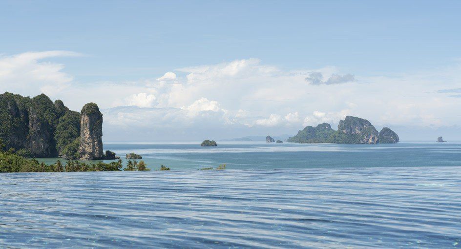 無邊際泳池的池緣連著遠方海面，海上有石灰岩島