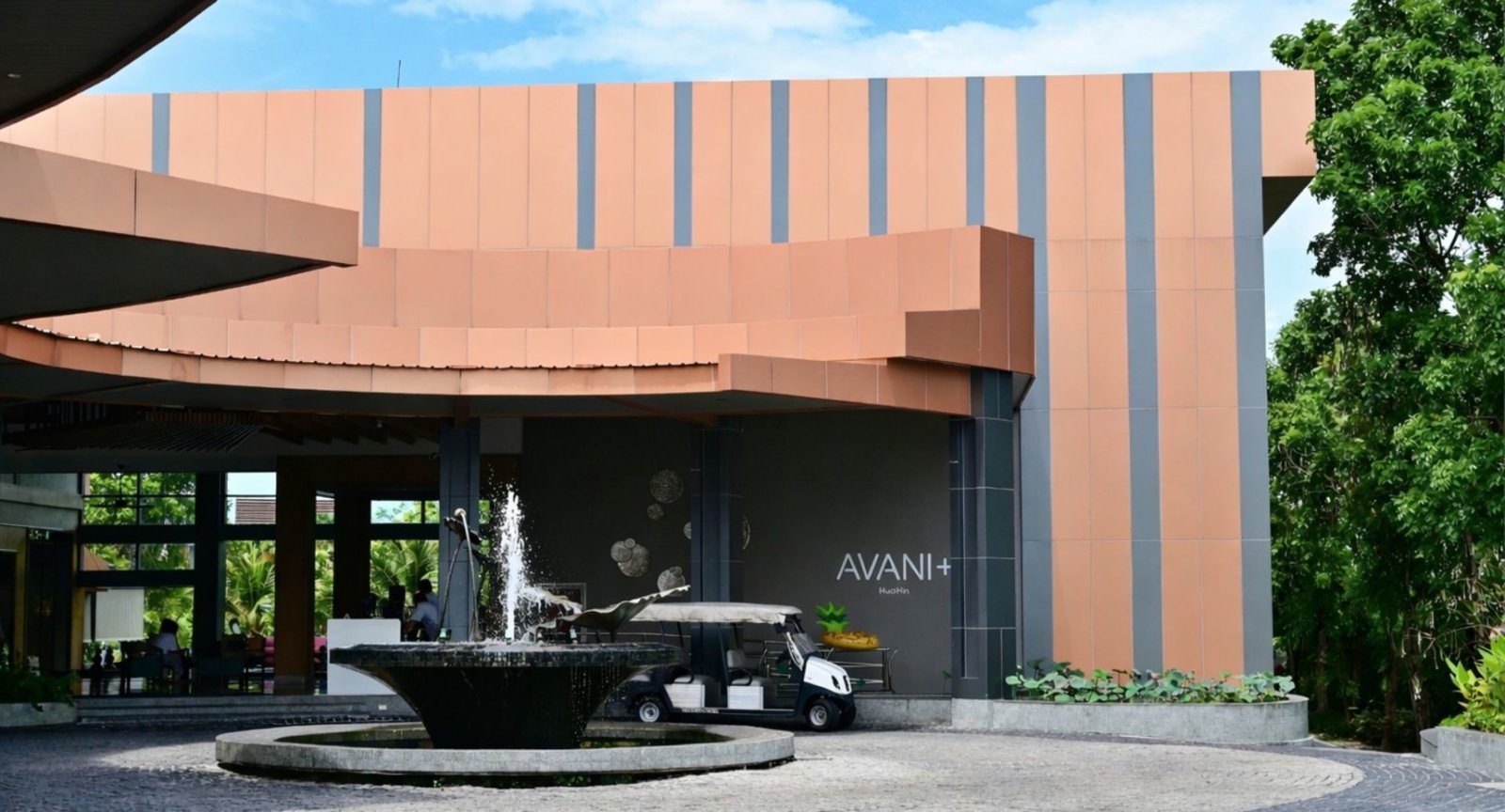度假村入口的弧形建築與噴水池，牆上掛著 AVANI+ 字樣