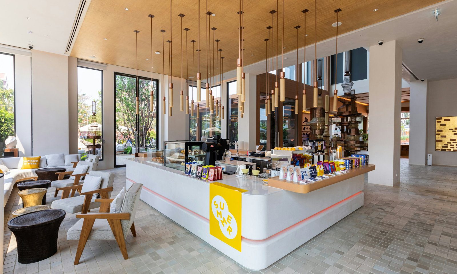 館內咖啡廳 The Summer Coffee 的白色吧台與成排吊燈，落地窗外是綠樹