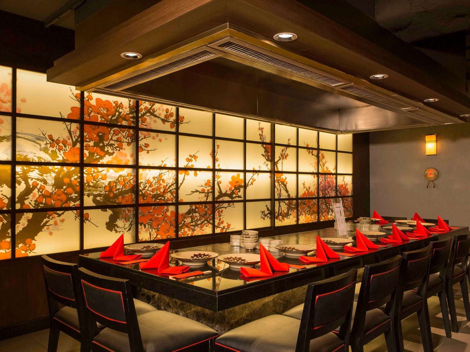 鐵板燒餐廳的長形鐵板桌與紅色餐墊，後方是暖黃燈光與木格屏風