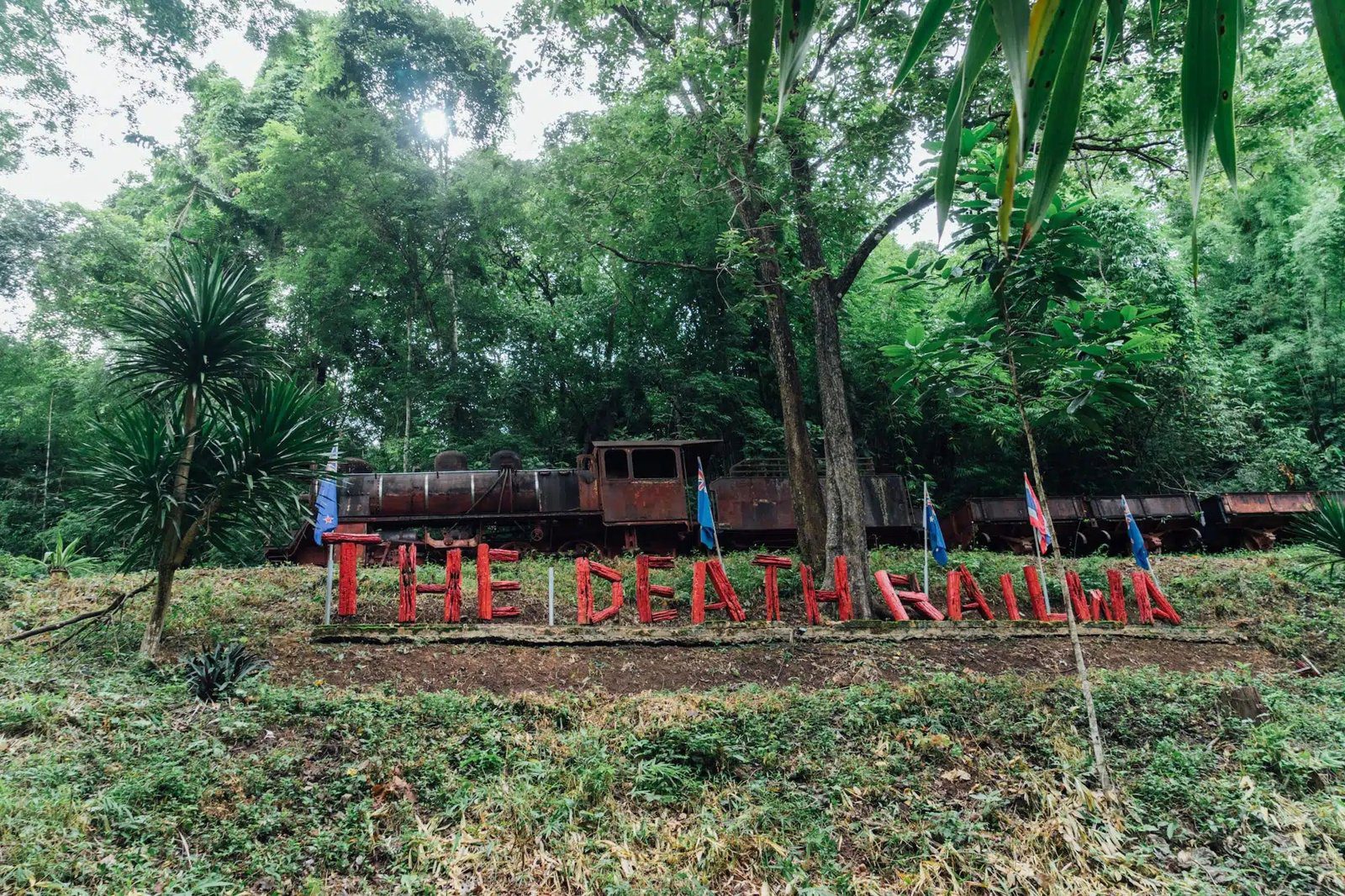 草地上立著紅色字牌，後方樹林裡停著一節舊火車車廂
