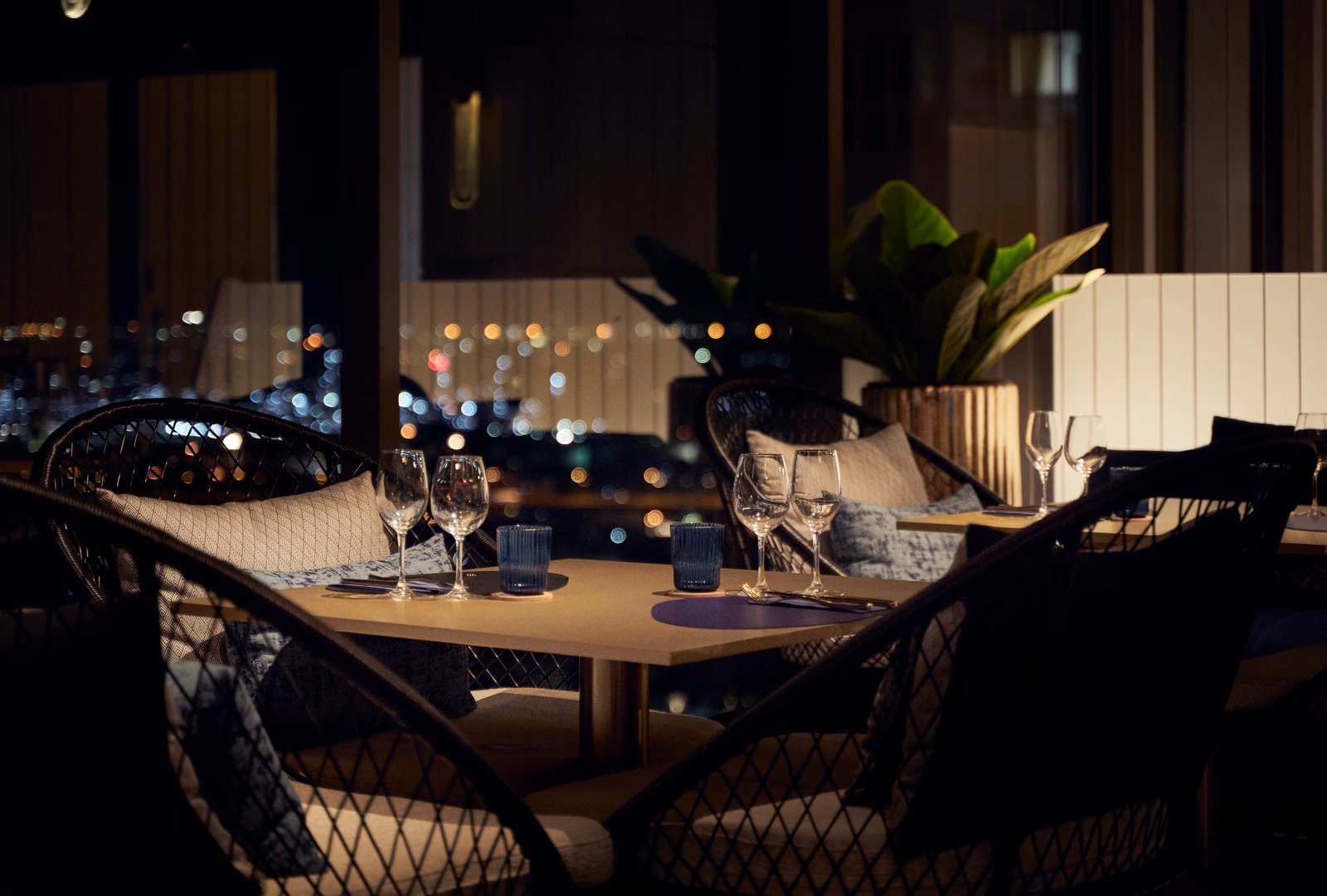 夜晚的餐廳窗邊座位，桌上擺著酒杯，窗外是點點城市燈火