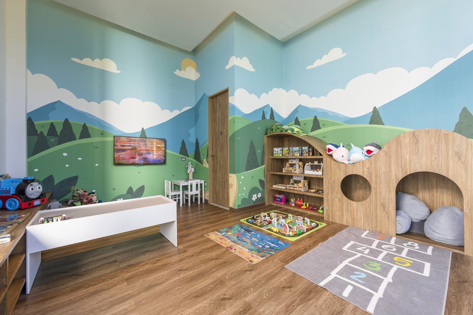 兒童遊戲室牆上畫著山景，擺著木製遊戲屋與玩具