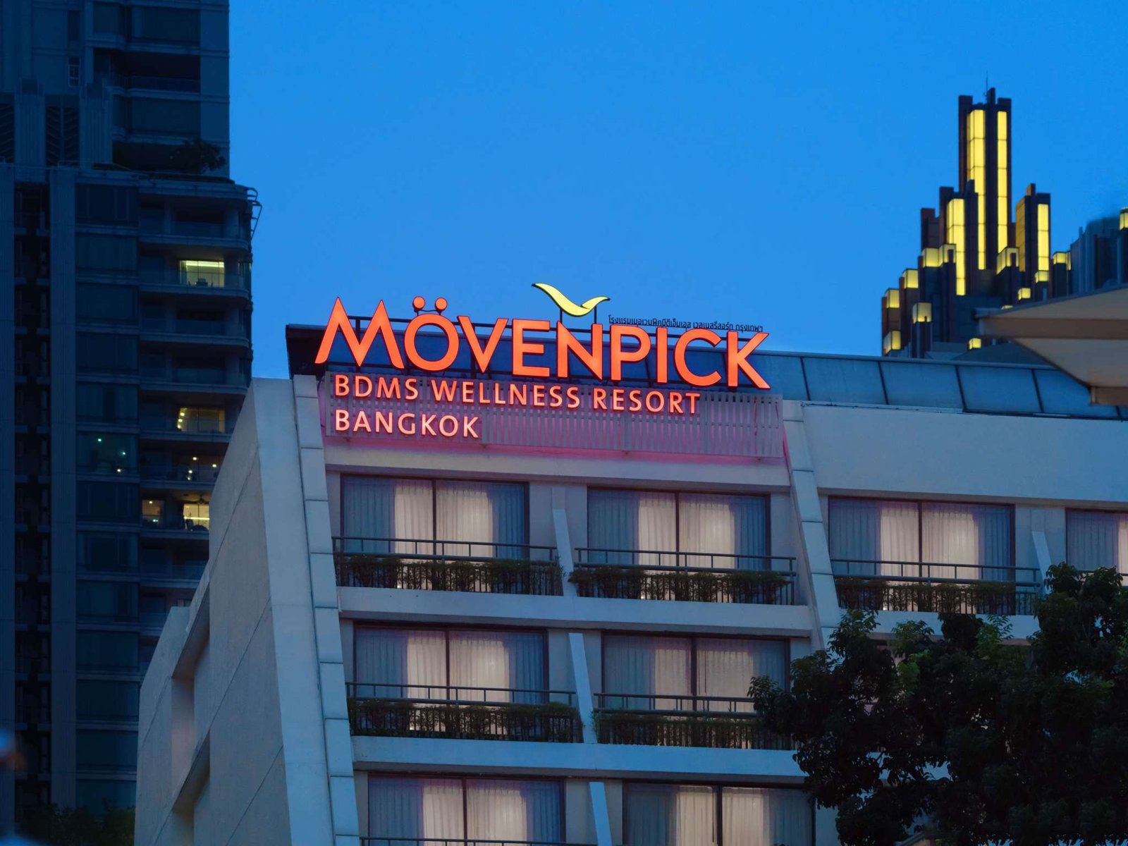 傍晚藍色天空下的飯店外觀，建築上方掛著紅色 MÖVENPICK 字樣，後方是高樓