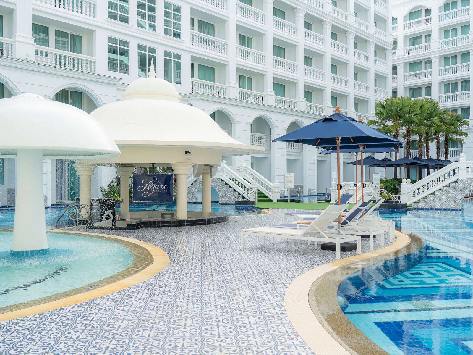 泳池邊白色傘形噴水裝置與圓頂的 Azure Pool Bar，藍白花磚池畔擺著躺椅與深藍陽傘