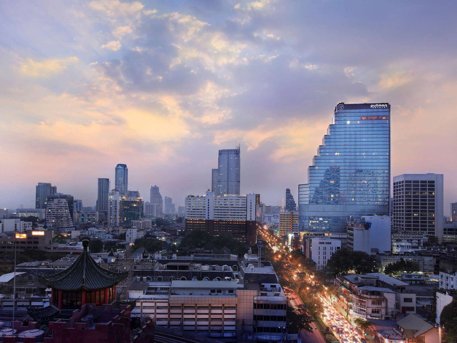 黃昏時從高處看是隆一帶街景，右側頂端掛著 G 字標誌的藍色玻璃大樓就是飯店，街上車燈連成一線