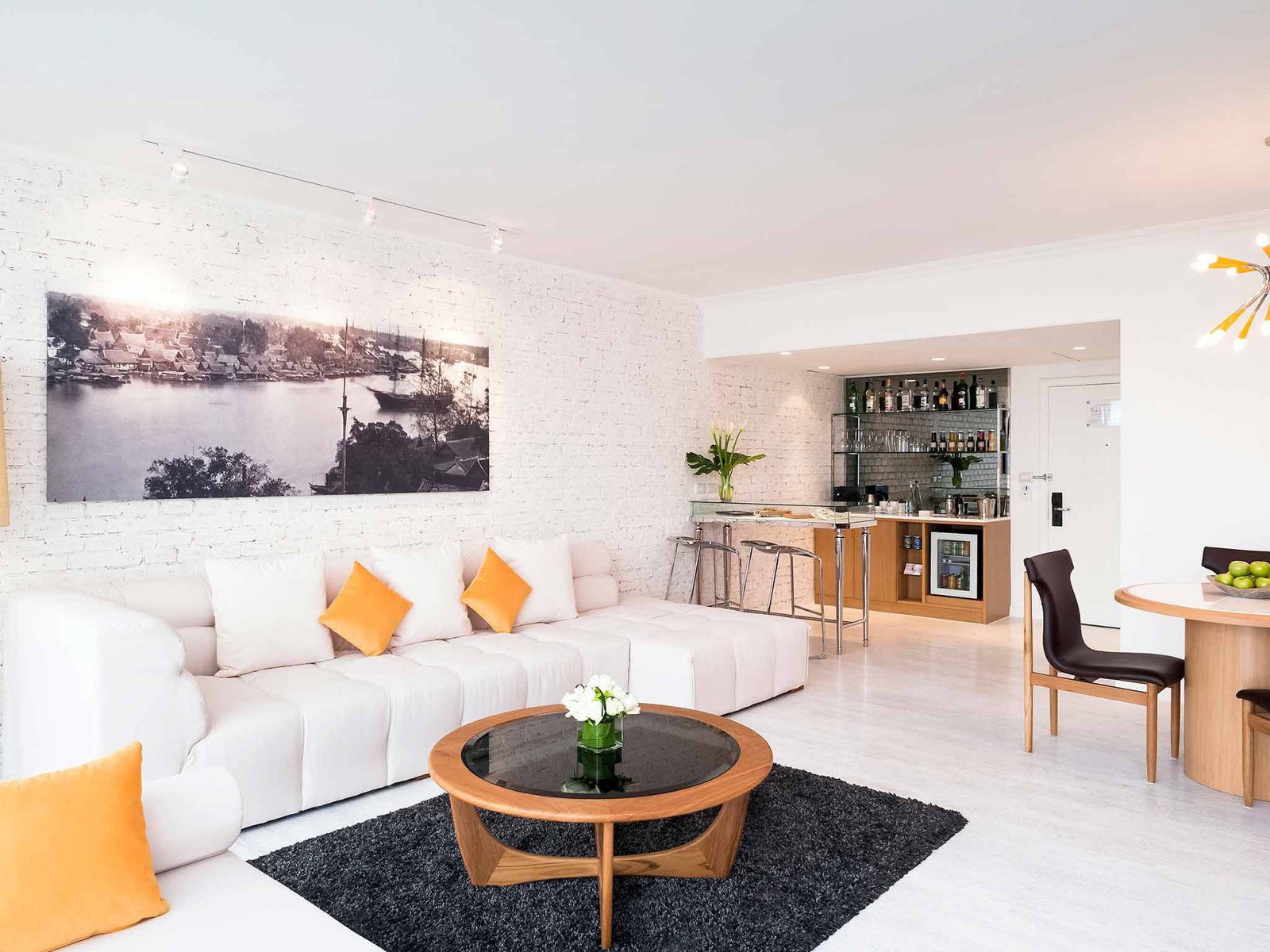 白色 loft 風格套房客廳，白磚牆掛著黑白河景照片，白色長沙發配橘色抱枕，一角是吧台