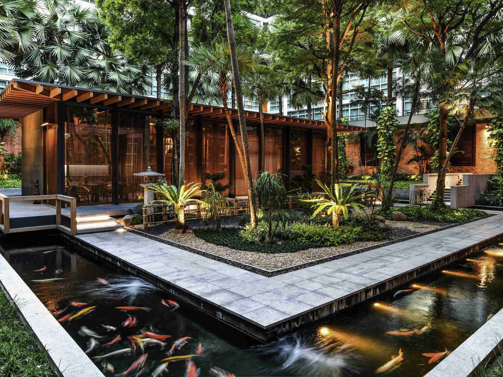 木造獨棟餐廳建在花園中，前方水池裡有錦鯉，四周是熱帶樹木