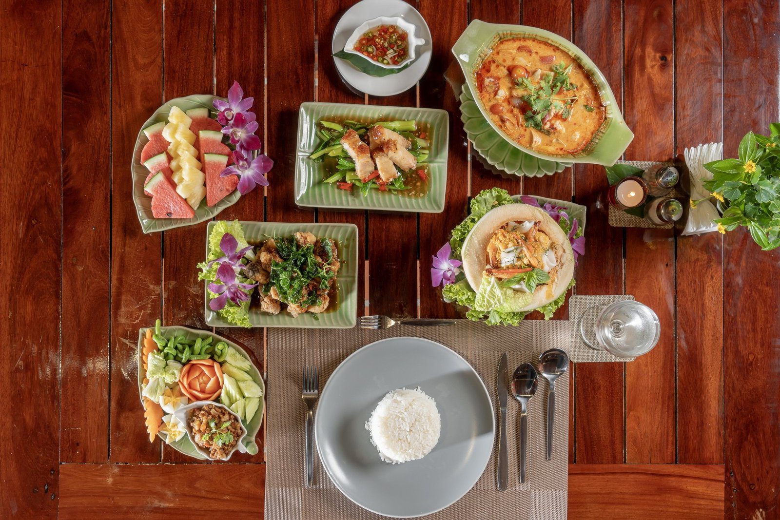 木桌上擺滿泰國菜，有咖哩、炒菜與沙拉，中間是一盤白飯
