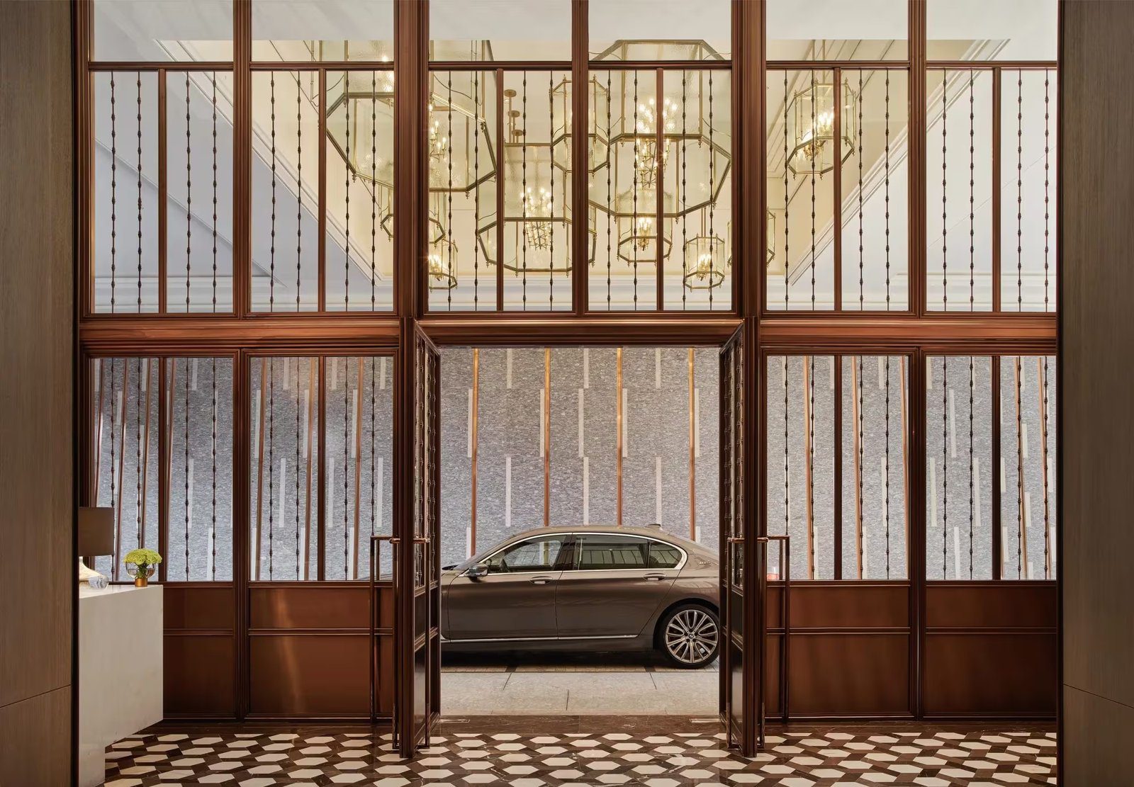 木框玻璃門後的車道門廊停著一輛深色轎車，地面是幾何花紋地磚