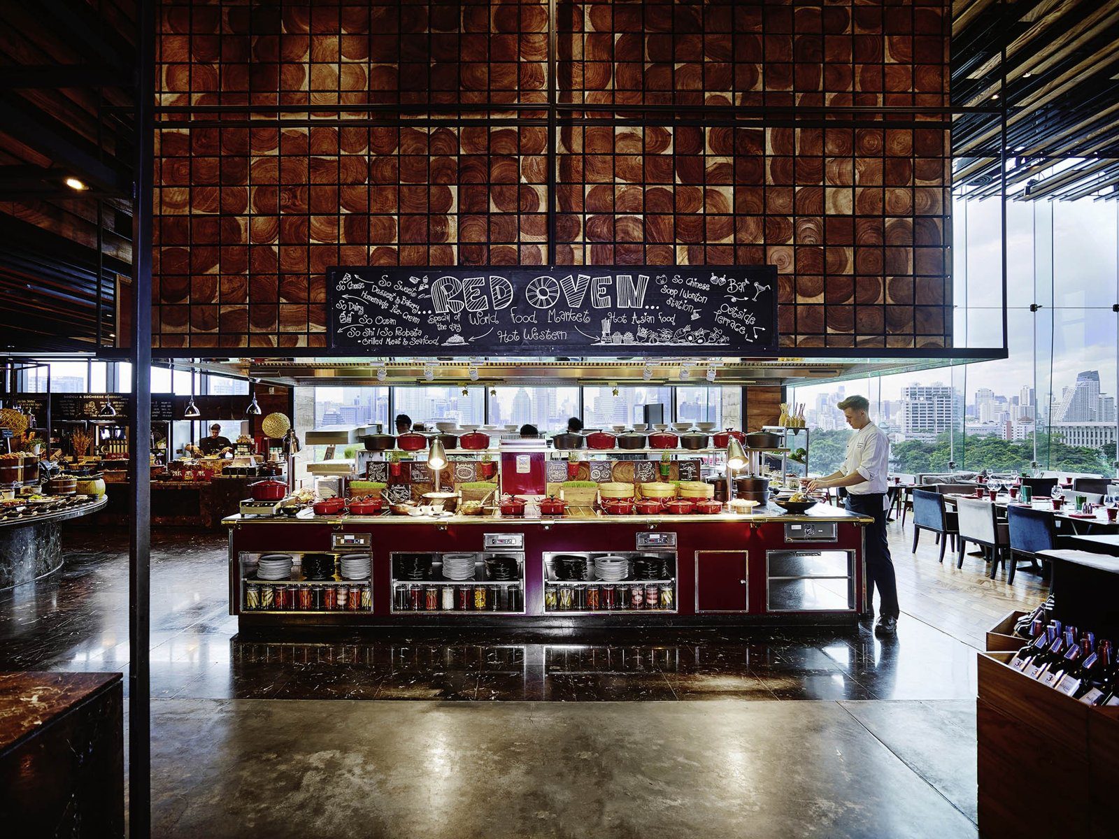 餐廳開放式廚房的紅色爐台與料理檯，上方黑板寫著 Red Oven，右側窗外是公園綠地