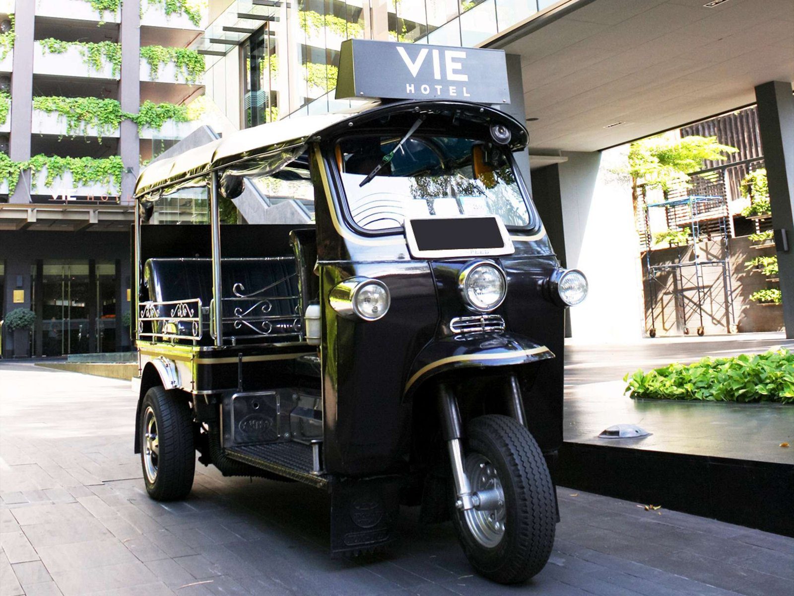 飯店門口停著一台車頂印有 VIE 字樣的黑色嘟嘟車