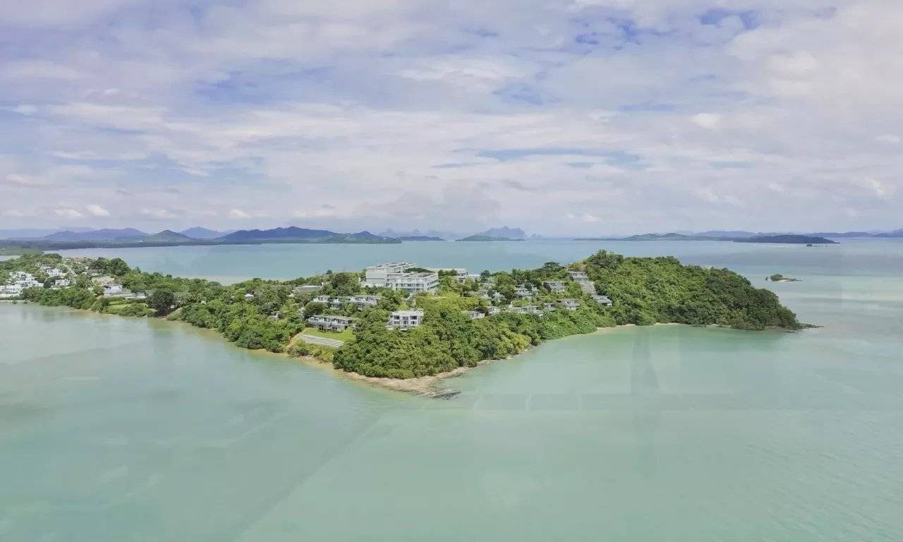 空拍伸入海灣的綠色岬角，岬上是白色度假村建築，遠方是攀牙灣島群