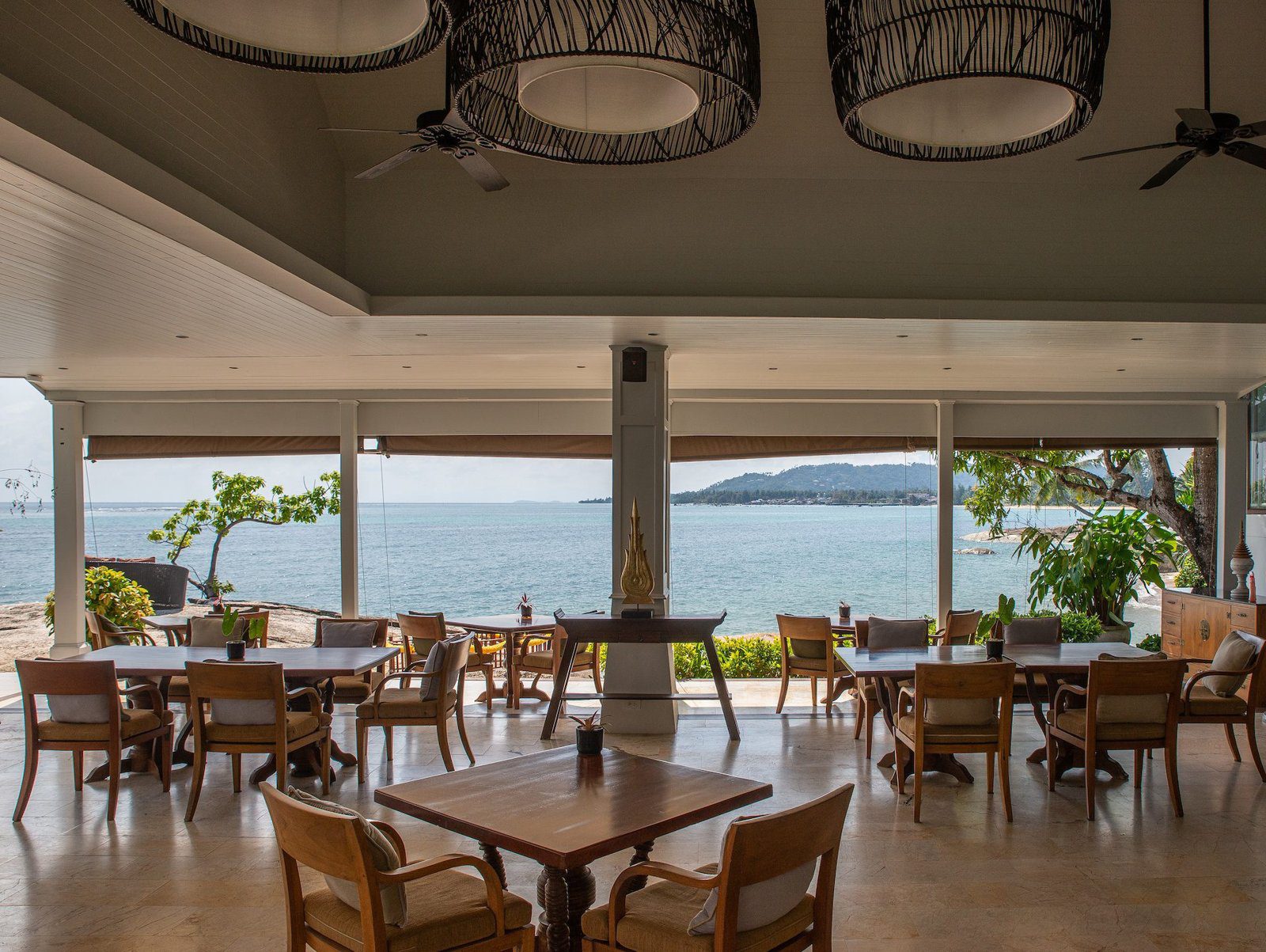 面海的開放式餐廳擺滿木桌椅，窗外是海灣與遠處島嶼