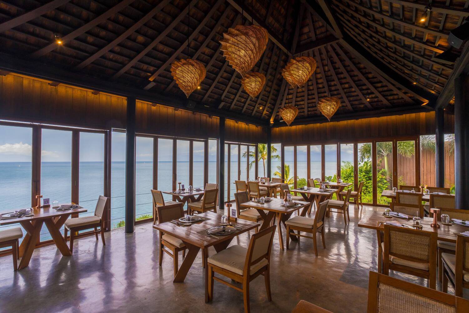 挑高木屋頂下的餐廳，落地窗外是海面與綠樹，桌椅排列整齊